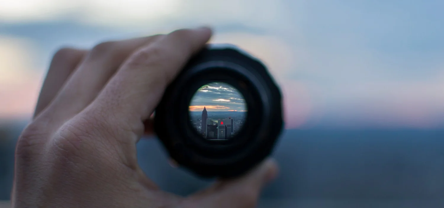 Hand holding binoculars up to a city skyline at sunset