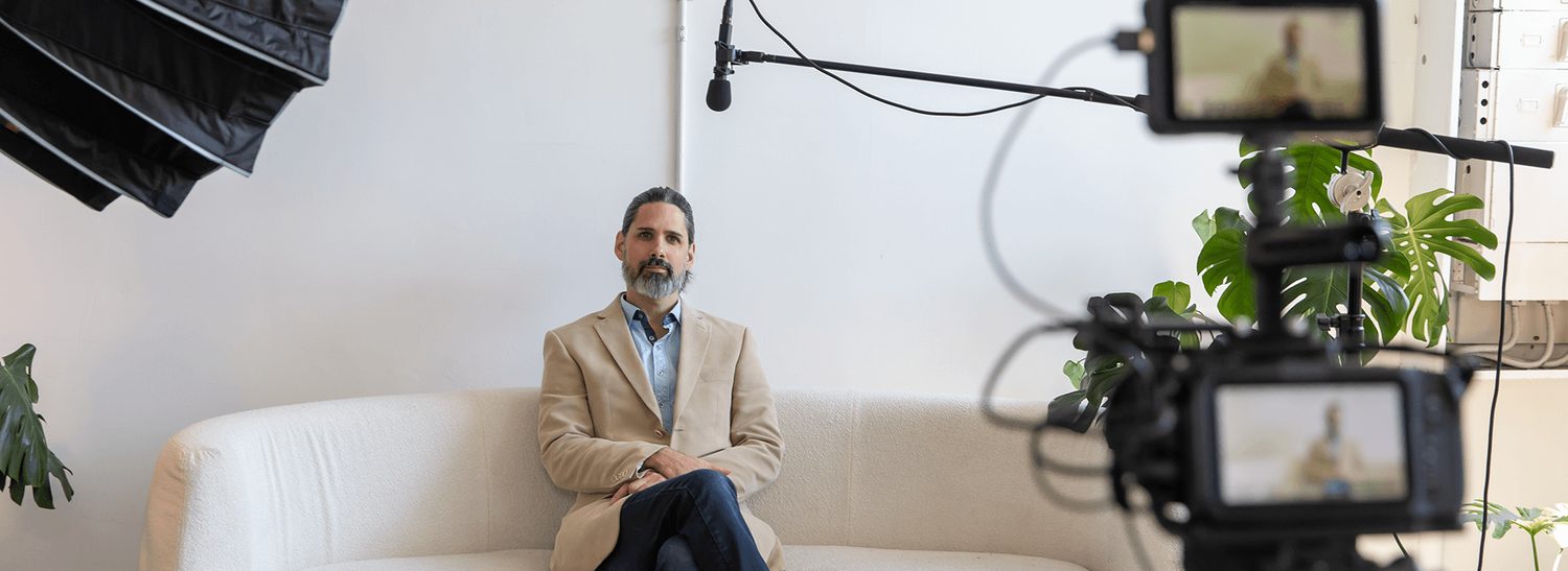 Interview setup for a corporate storytelling video, with a speaker seated on a sofa and cameras, lighting, and boom microphone visible