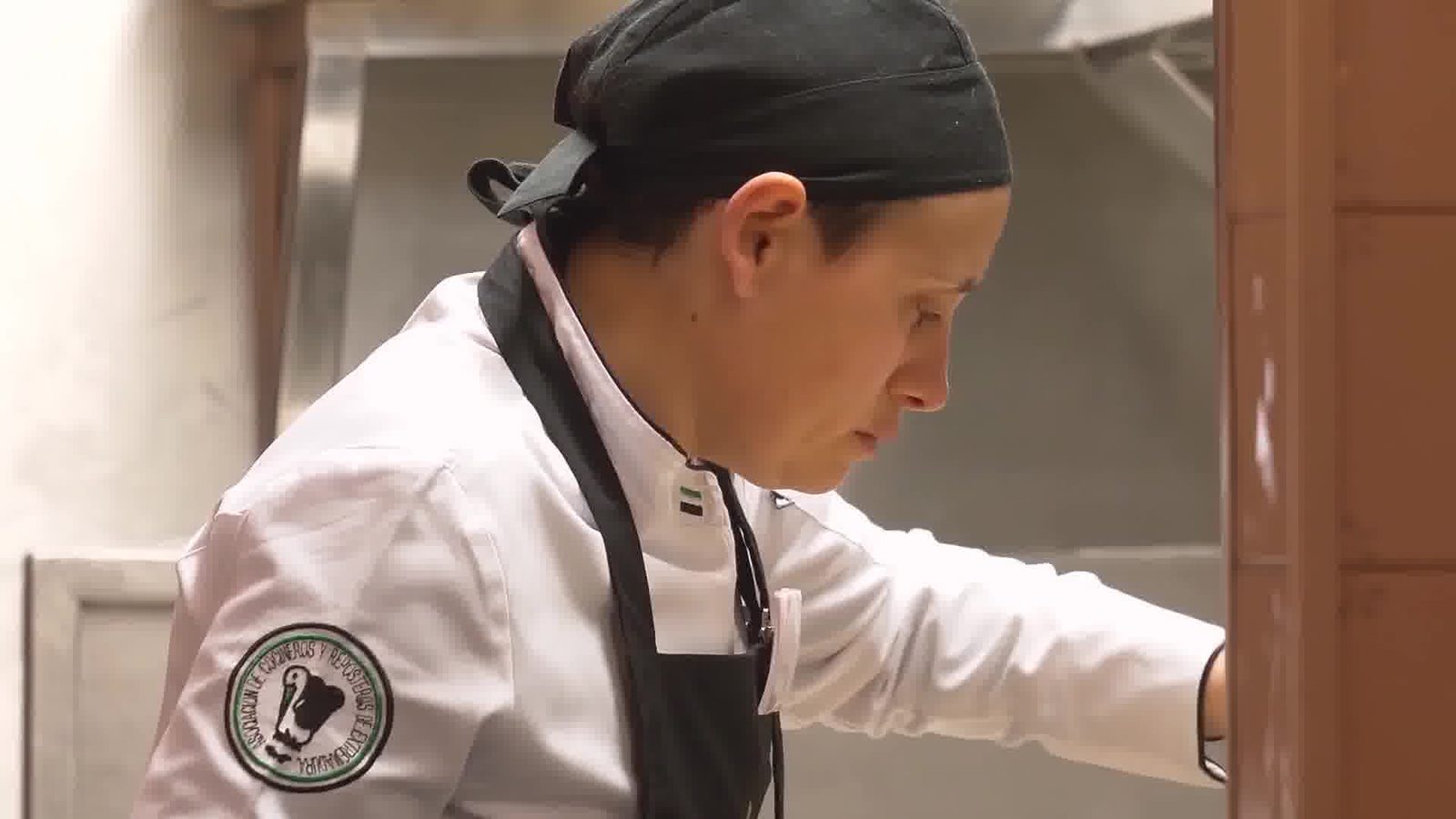 A chef in whites and a dark bandana concentrates on his work in a professional kitchen