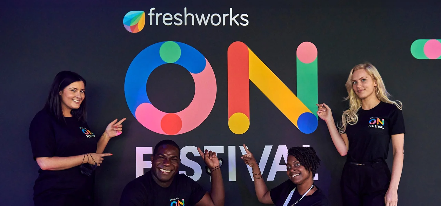 Four people smiling in front of a Freshworks ON Festival backdrop