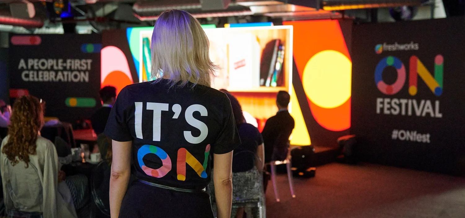 A woman with her back to the camera, wearing an IT'S ON T-shirt, watching the stage at ON Festival
