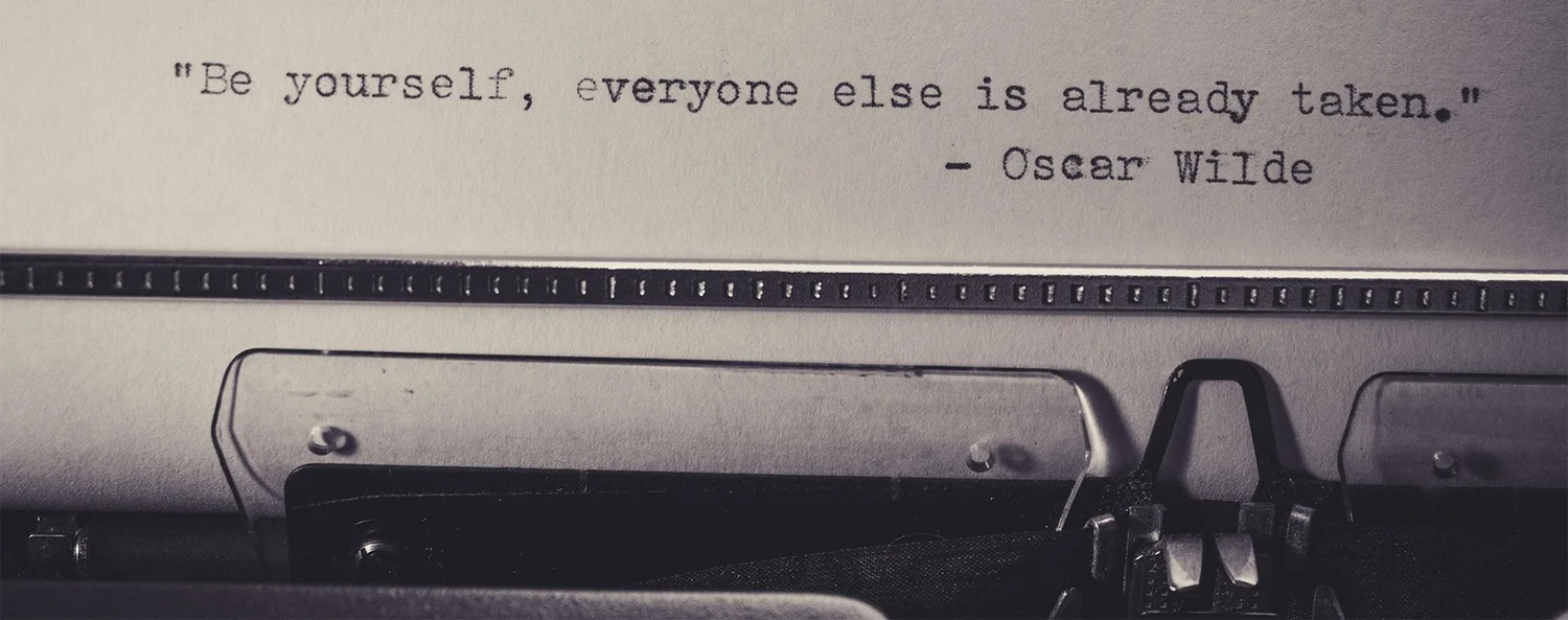 A vintage typewriter in black and white, its paper reading “Be yourself; everyone else is already taken.” (Oscar Wilde)