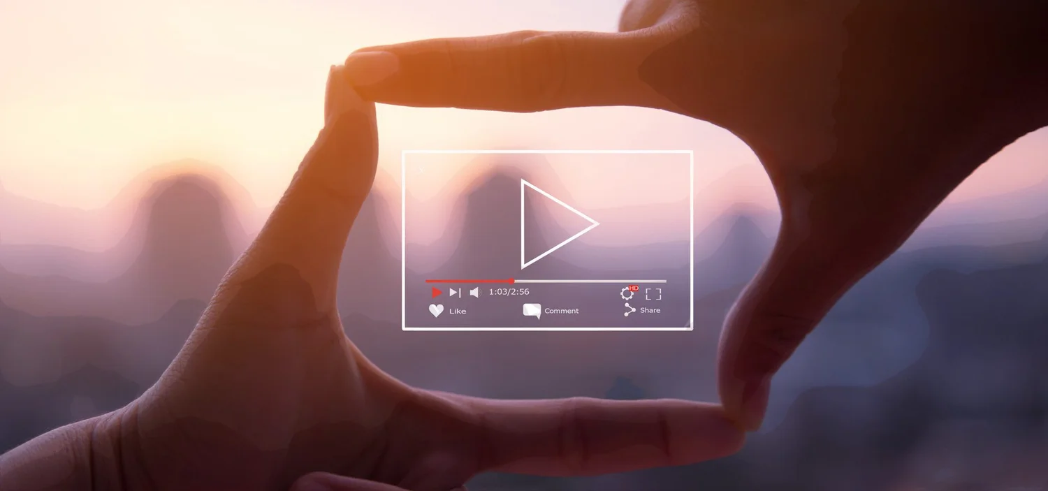 Hands making a frame around a video player graphic against a sunset sky