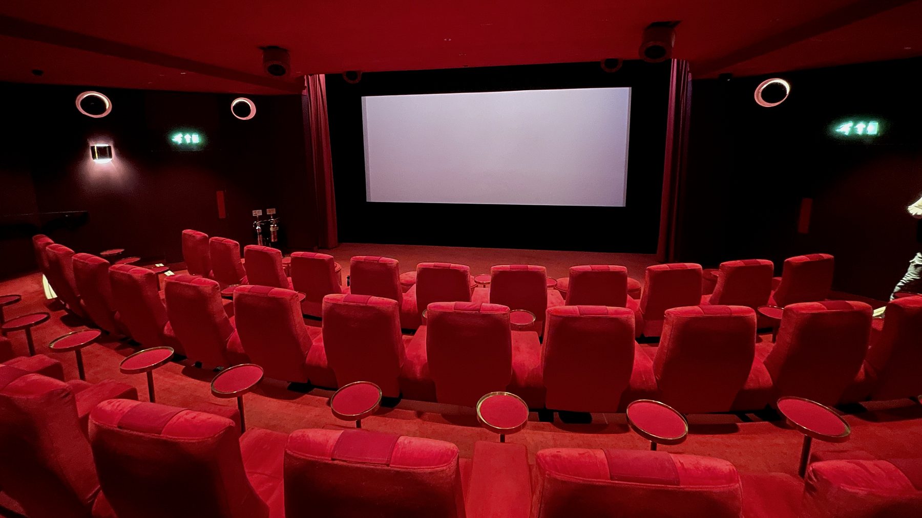 An empty cinema with rows of red seats facing a blank screen