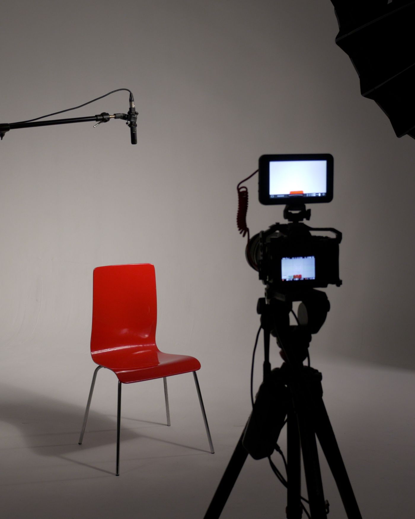 Interview set ready for filming: a red chair, a boom mic, a camera and a softbox